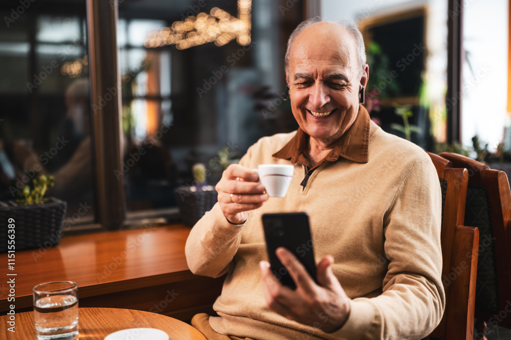 Happy senior man drinking coffee while using mobile phone and earphones. He is relaxing in the cozy city bar at evening and using technology. Happy senior man drinking coffee while using mobile phone and earphones. He is relaxing in the cozy city bar at evening and using technology.