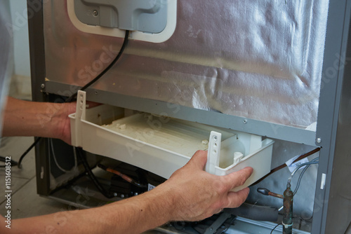 man takes Compressor tray with water from refrigerator, defrosting refrigerator, tray for collecting melted water in refrigerator