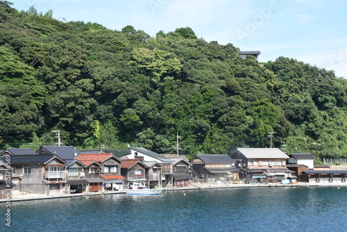 Traditional wooden boathouses, called funaya, line the water in Ine, Japan. These unique homes have storage for boats below and living spaces above, blending practicality with rustic charm. photo