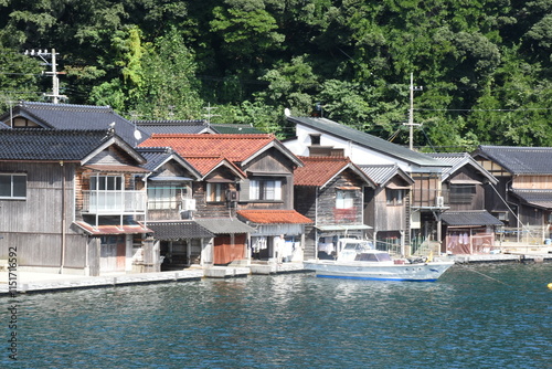 Traditional wooden boathouses, called funaya, line the water in Ine, Japan. These unique homes have storage for boats below and living spaces above, blending practicality with rustic charm. photo