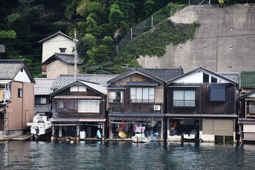 Traditional wooden boathouses, called funaya, line the water in Ine, Japan. These unique homes have storage for boats below and living spaces above, blending practicality with rustic charm. photo