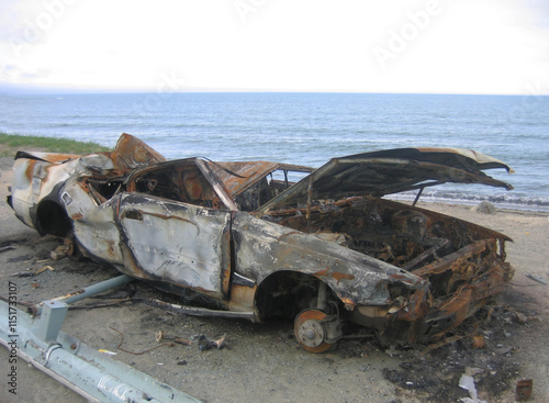 A burnt-out car on the seashore.
The island of a completely burnt-out car stands on the seashore. The car was badly damaged by fire, windows were missing, and the metal was deformed and charred.