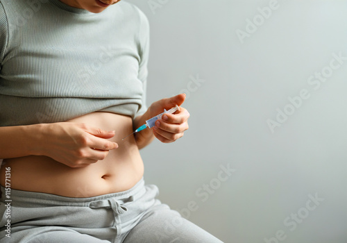 Woman administering medication to her abdomen while seated in a neutral-toned room during the day