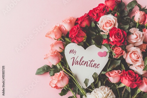 flat lay pink and red roses arranged in a shape of a heart, paper card on top of roses with text "my Valentine" in beautiful cursive, pink solid color background
