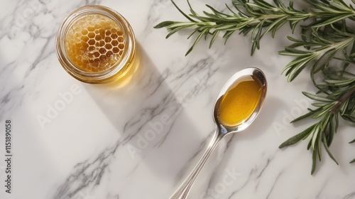 A silver spoon with honey placed next to a jar of honeycomb and sprigs of fresh rosemary on a marble surface
