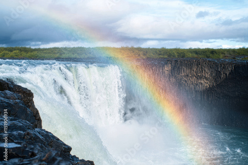 stunning waterfall with vibrant rainbow arching over it, surrounded by lush greenery and dramatic clouds