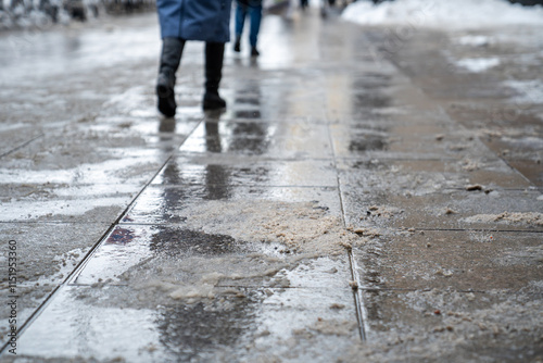 Anti-icing chemicals in winter season. People walking on the street treated with technical salt or de-icing chemicals. Effective tool to fight ice on surfaces. Rock salt on road. 