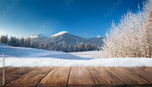 empty wooden table top coverd with snow with reproduction area and wintry weather snowing bushes and mountain background photo