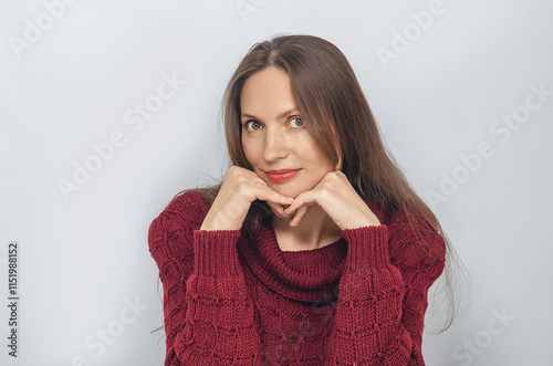 Portrait of woman looking flirtatiously, wearing a red knitted sweater. Hands under chin, long hair.