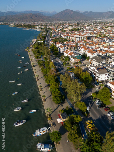 A bike path through the trees. A coastal path right next to the sea. Parked boats. Buildings built next to the coastal path.
