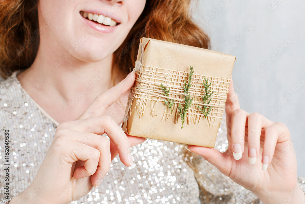 Woman holds a Christmas gift decorated with thuja twigs.