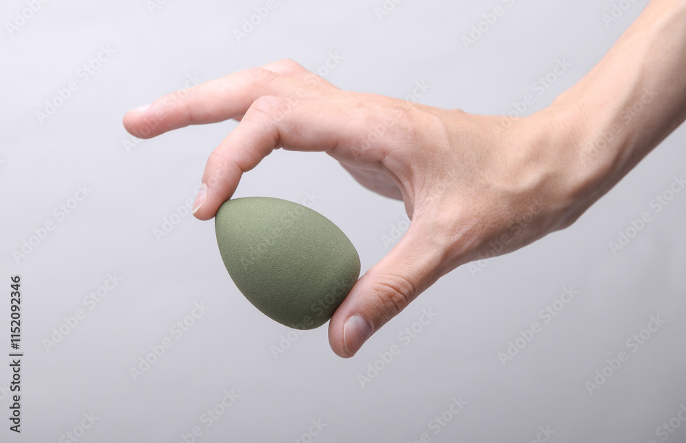 Female hand holding makeup sponge on gray background Female hand holding makeup sponge on gray background