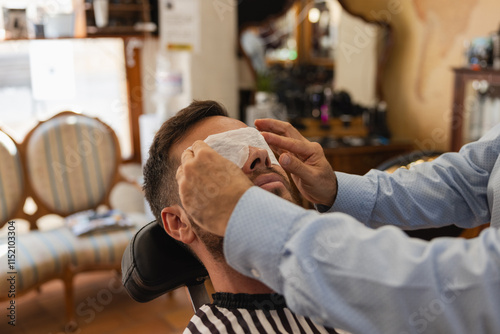 A man is getting his face shaved by another man