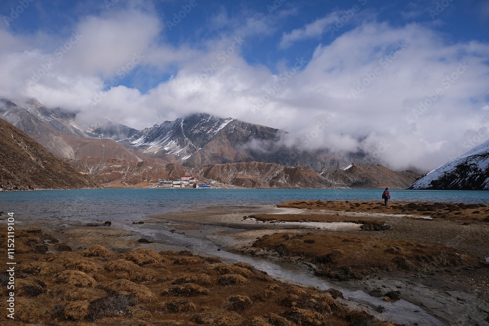 Φωτογραφία Stunning panorama of Gokyo with single person on coast of turquoise lake among mountains and buildings of settelment on horizon