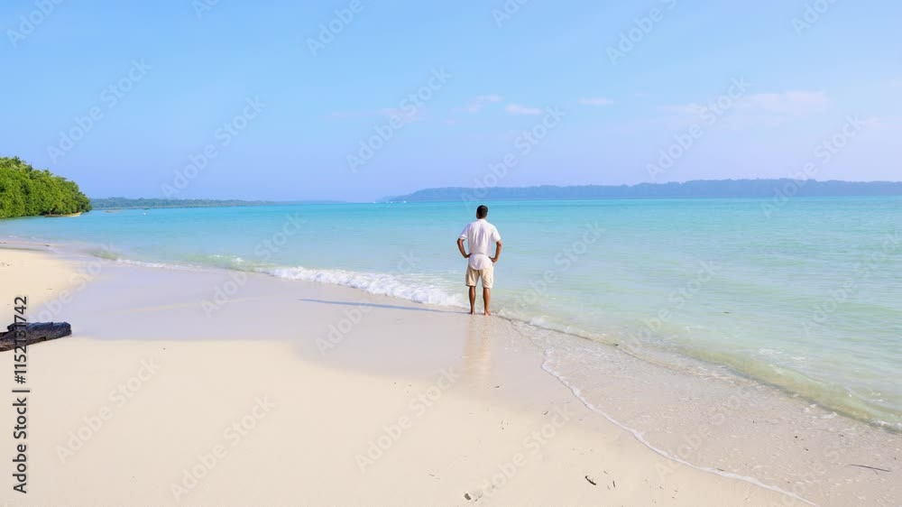 isolated man standing at pristine white sand beach with rolling sea waves at morning from top angle isolated man standing at pristine white sand beach with rolling sea waves at morning from top angle