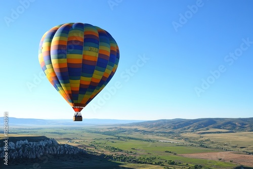 vibrant hot air balloon rising into clear blue sky over sprawling green valley photo