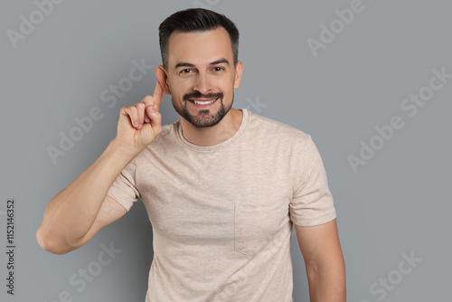 Man showing hand to ear gesture on grey background