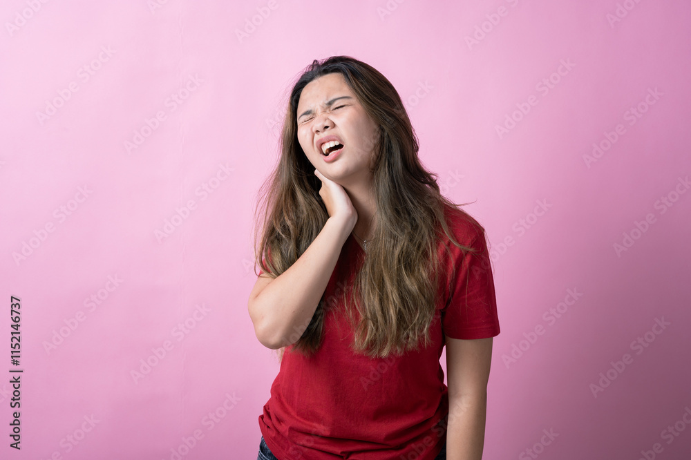 Asian woman in a red shirt with long brown hair grimaces in pain, holding the back of her neck with one hand, against a solid pink background. Asian woman in a red shirt with long brown hair grimaces in pain, holding the back of her neck with one hand, against a solid pink background.