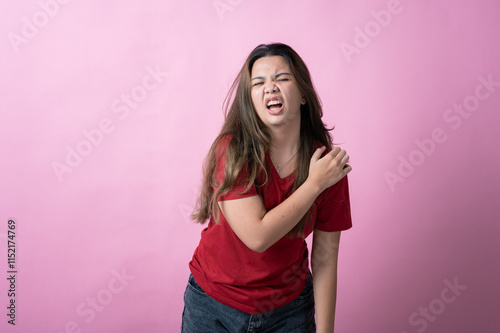 Wallpaper Mural Asian woman in a red shirt with long brown hair grimaces in pain while holding her shoulder, standing against a solid pink background. Torontodigital.ca