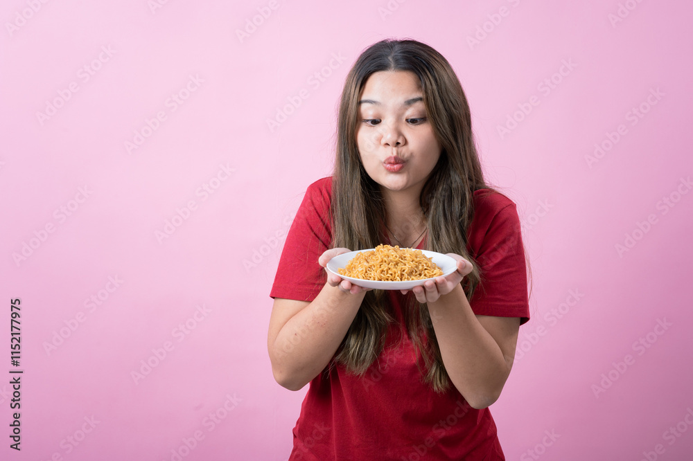 Surprised young woman with long brown hair wearing a red t-shirt, holding a white plate filled with instant noodles, posing against a pink background. Perfect for food related concepts. Surprised young woman with long brown hair wearing a red t-shirt, holding a white plate filled with instant noodles, posing against a pink background. Perfect for food related concepts.