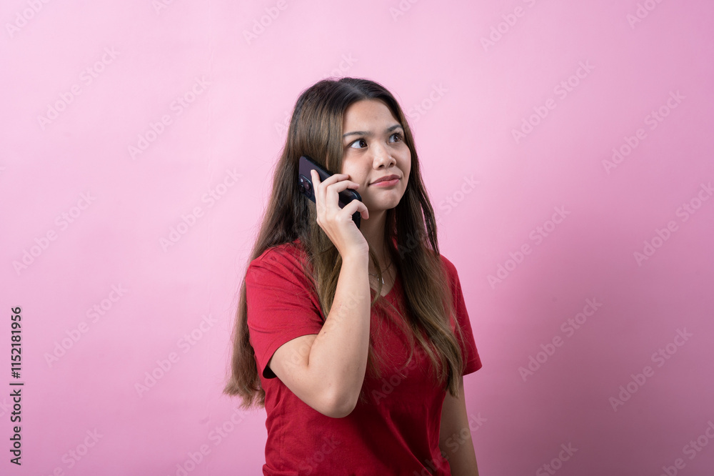 Surprised young woman with long brown hair wearing a red t-shirt talks on a smartphone against a pink background, reacting with shock or excitement during a phone call, expressing strong emotions. Surprised young woman with long brown hair wearing a red t-shirt talks on a smartphone against a pink background, reacting with shock or excitement during a phone call, expressing strong emotions.