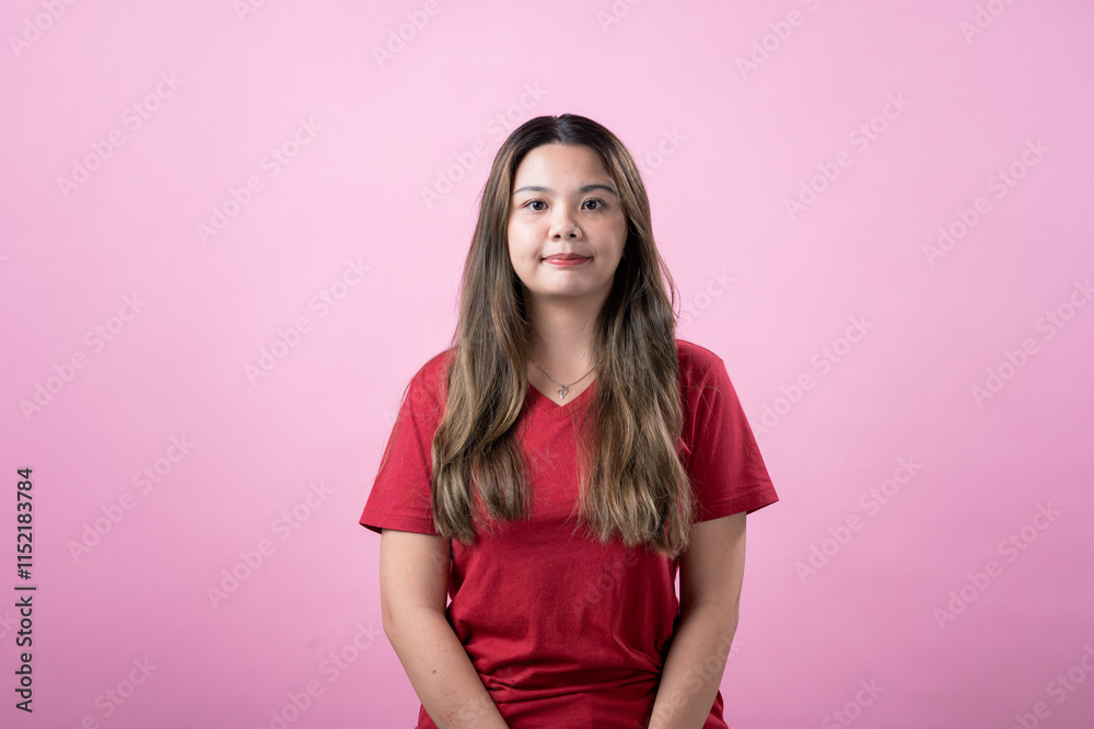 Asian woman with long, straight brown hair wearing a red t-shirt sitting against a pink background, looking calm and confident, showcasing natural beauty, simplicity, and a relaxed demeanor. Asian woman with long, straight brown hair wearing a red t-shirt sitting against a pink background, looking calm and confident, showcasing natural beauty, simplicity, and a relaxed demeanor.