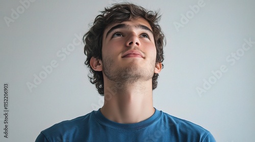Young Man Gazing Upward in Solid Blue Shirt Against Plain Background