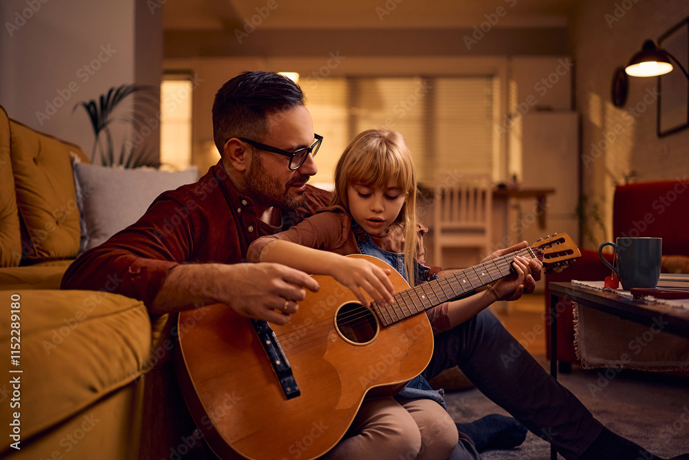 Obraz premium Little girl learning to play acoustic guitar with help of her father at home.