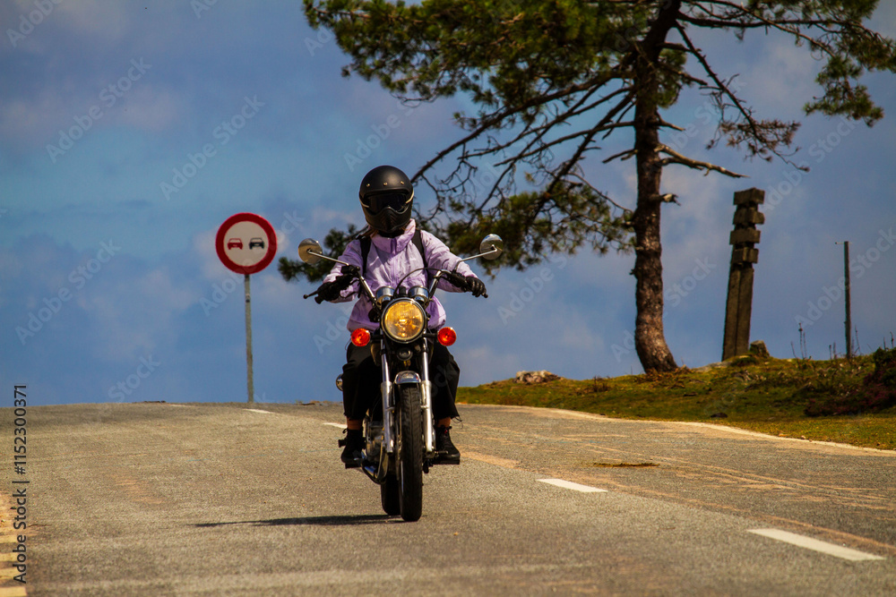 Obraz premium Primer plano de una chica motociclista avanzando por una carretera rural con un cartel de prohibido adelantar al fondo.