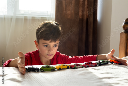 A young boy, aged 6-8, plays with toy cars in a sunny, cozy room, aligning them in a row. The scene highlights themes of autism, developmental disorders, childhood play, and mental well-being.