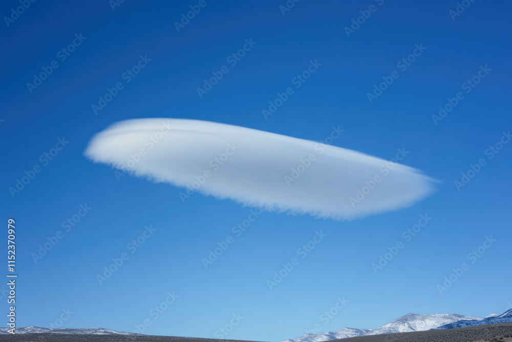 Lenticular cloud hovering above snow-covered mountains in clear blue sky Lenticular cloud hovering above snow-covered mountains in clear blue sky