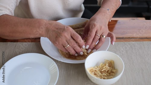 Woman wraps shredded chicken in tortilla to prepare enchiladas