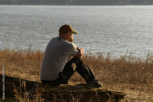Hiking and camping outdoorsman sitting near lake watching the setting sun