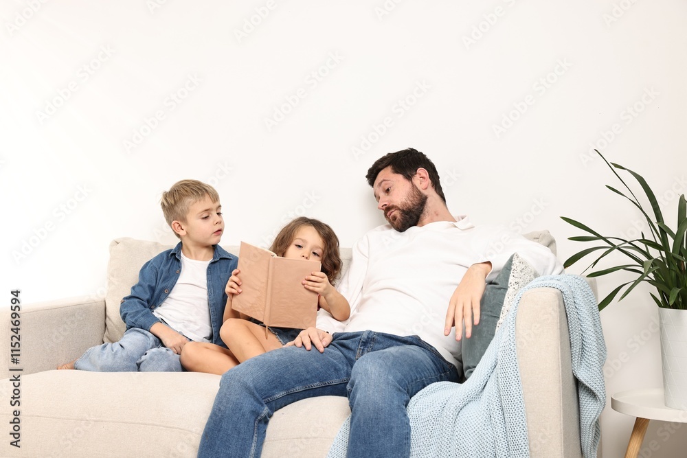 Overwhelmed father and his children reading book on sofa at home Overwhelmed father and his children reading book on sofa at home