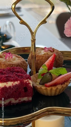 Tea time, traditional English tea ceremony with Afternoon tea cakes, sandwiches and teapot with hot tea. Sweet tasty cakes and desserts with greenery on background.