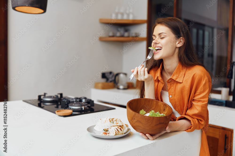 Young woman enjoying healthy salad in a modern kitchen, smiling and dressed in an orange shirt, promoting healthy eating and lifestyle choices Young woman enjoying healthy salad in a modern kitchen, smiling and dressed in an orange shirt, promoting healthy eating and lifestyle choices