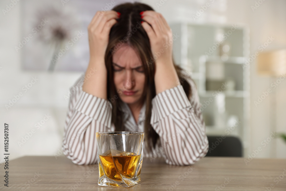 Alcohol addiction. Woman at wooden table indoors, focus on glass of whiskey Alcohol addiction. Woman at wooden table indoors, focus on glass of whiskey