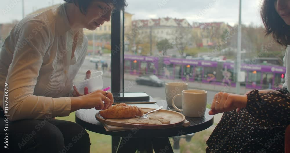 Two individuals are delightfully enjoying their coffee and fresh croissants at a cozy cafe table with a Window View