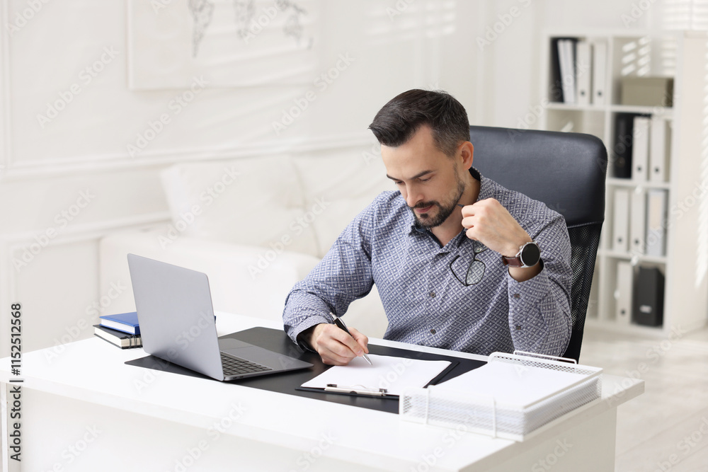 Handsome banker signing document at table in office Handsome banker signing document at table in office