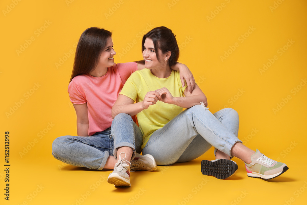 Portrait of happy twin sisters on orange background