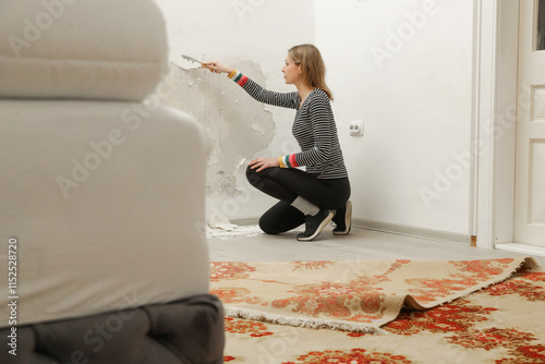 Saltpeter or mold on the wall problem. Woman is using a scraper to scrape and remove all loose paint and plaster that is in poor condition, until a firm surface is achieved. photo