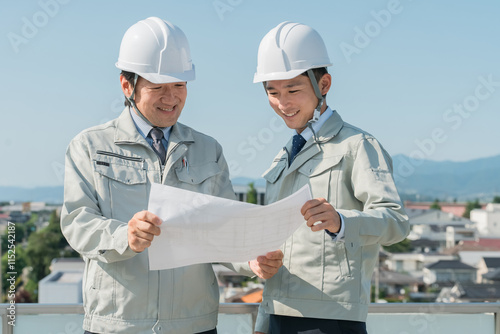 Naklejka 青空で設計図を見る作業服を着た作業員（建設・建築・設計・不動産・土木・工事・現場監督） 
