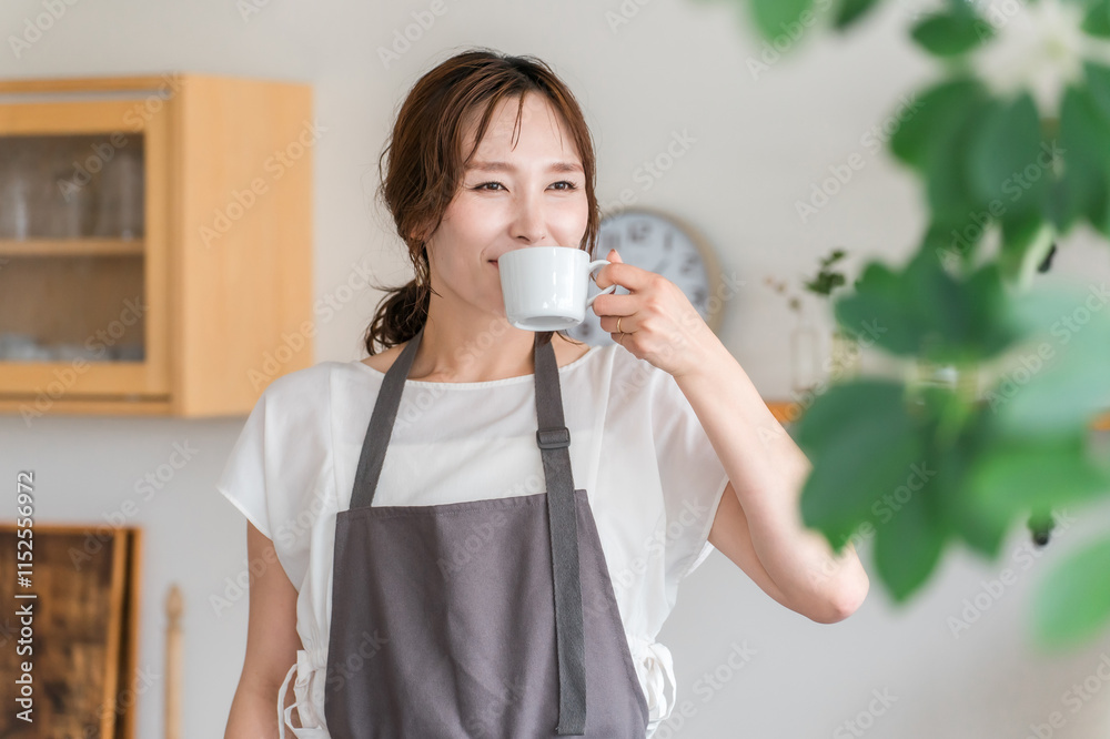 キッチン・ダイニングでコーヒーを飲むエプロン姿の若いアジア人女性
