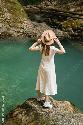 Woman in white dress exploring nature standing on a rock near turquoise water