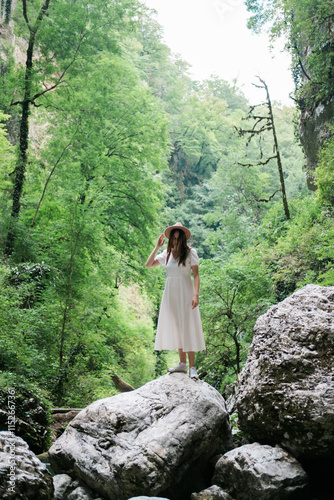 Woman in white dress standing on a rock in a lush green forest