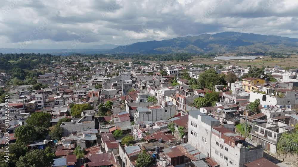 Aerial view of a small town with compact buildings, surrounded by lush greenery and mountains under cloudy skies. Video shot in Ciudad Antigua, Guatemala. Aerial view of a small town with compact buildings, surrounded by lush greenery and mountains under cloudy skies. Video shot in Ciudad Antigua, Guatemala.