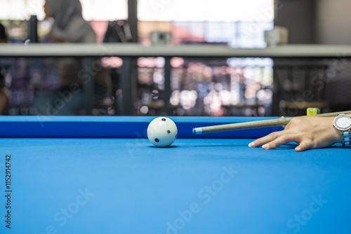 A hand strikes a billiard ball with precision using a cue stick during an intense pool game on a blue table, highlighting focus, skill, and competitive gameplay in an indoor setting. photo