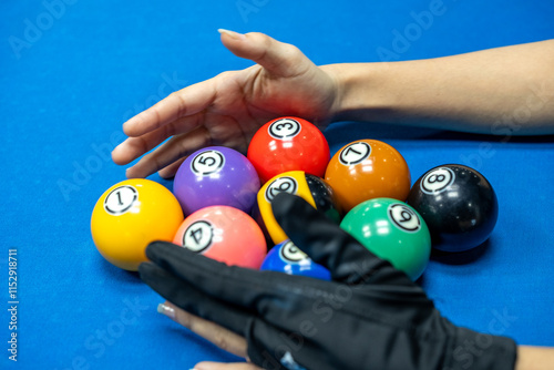 Close-up photo of a hand arranging colorful billiard balls in preparation for a 9-ball match on a bright blue pool table, emphasizing focus, precision, and the vibrant game atmosphere. photo