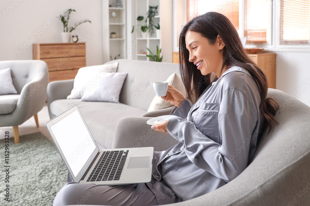 Young woman in grey pajamas with coffee and laptop working on armchair at home Young woman in grey pajamas with coffee and laptop working on armchair at home
