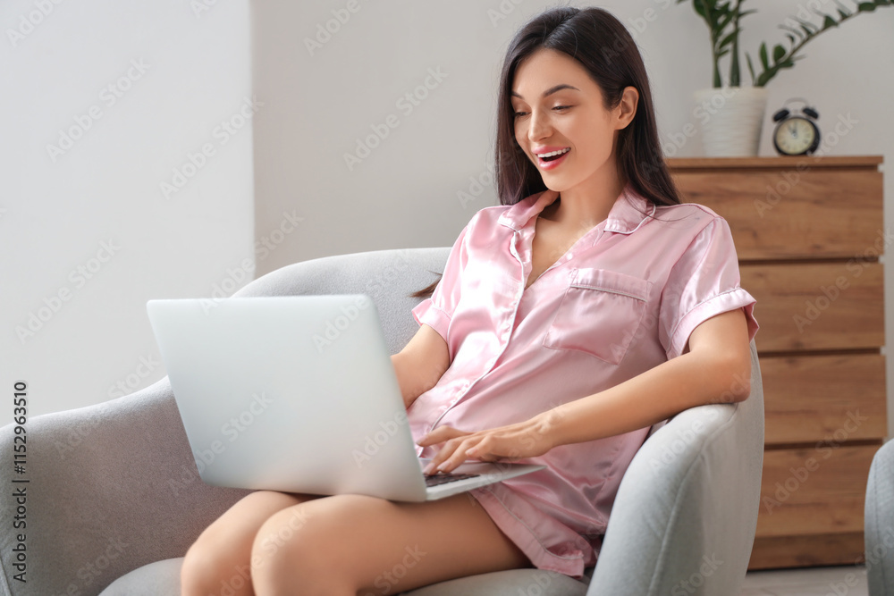 Female freelancer in pink pajamas working with laptop on armchair at home Female freelancer in pink pajamas working with laptop on armchair at home